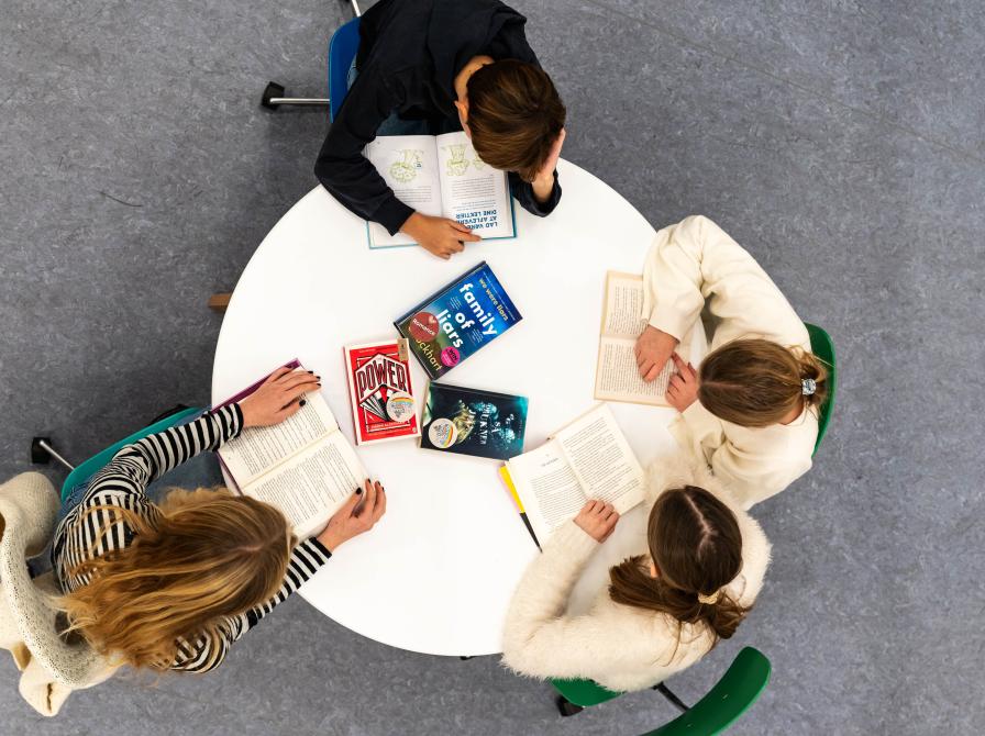 Fire børn der sidder omkring et bord med bøger og læser