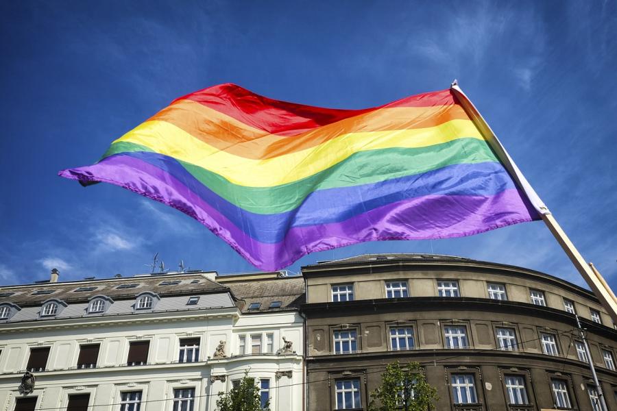 Foto af Prideflag (regnbueflag) taget nedefra med byhus i baggrunden
